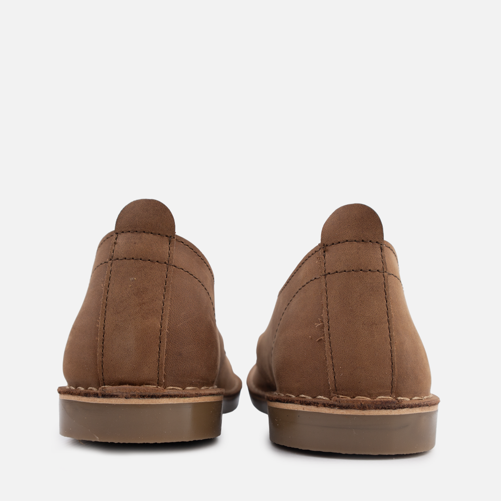 A pair of brown suede chukka leather shoes shown from the back, featuring stitched seams, a pull tab, and a brown rubber sole, set against a plain light gray background.