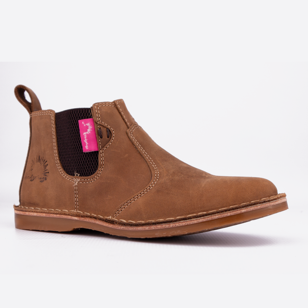 A single brown suede Chelsea boot shown in profile against a clean white background. The boot features a pull tab, elastic side gore, contrast stitching, and a pink brand tag on the side.