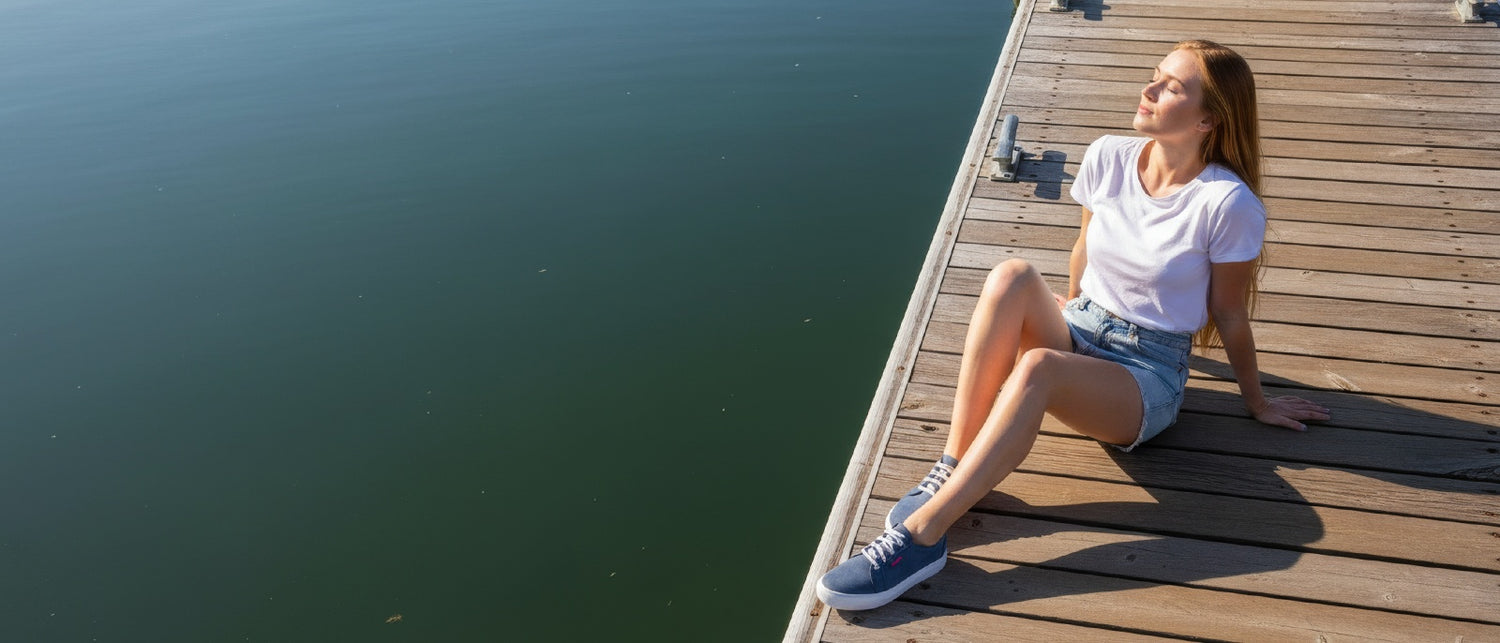 Woman sitting on a wooden dock by a body of water wearing Hedgehogs sneakers