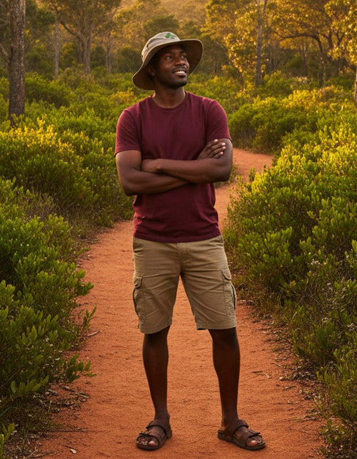 Man wearing Wolf Rock hat standing on a dirt path in a natural setting with trees and bushes.