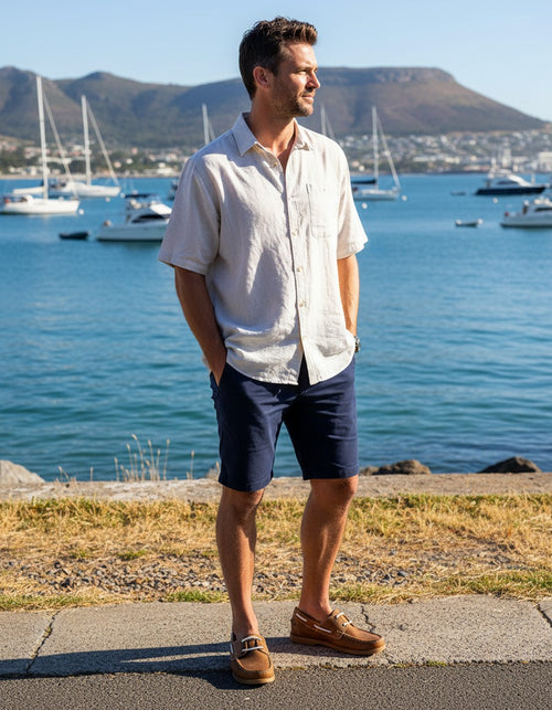 Man wearing Wolf Rock boat shoes standing by a waterfront with sailboats and mountains in the background