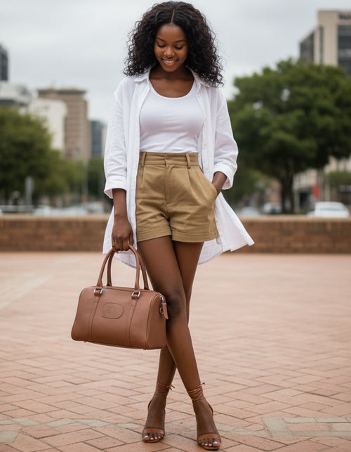Woman in white blazer and beige shorts holding a brown Hedgehogs handbag on a city street.