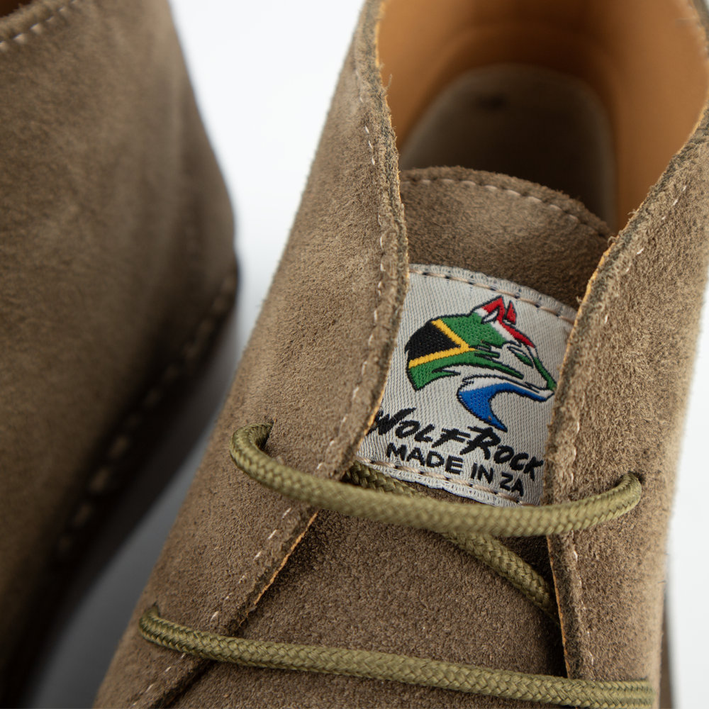 Close-up of a suede chukka shoe in olive-green with olive green laces, showing the embroidered Wolf Rock Made in ZA label on the tongue.