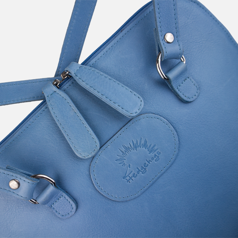 Close up view of the Hedgehogs ladies convertible backpack in baby blue leather, showing the front logo embossing and double zip closure. 