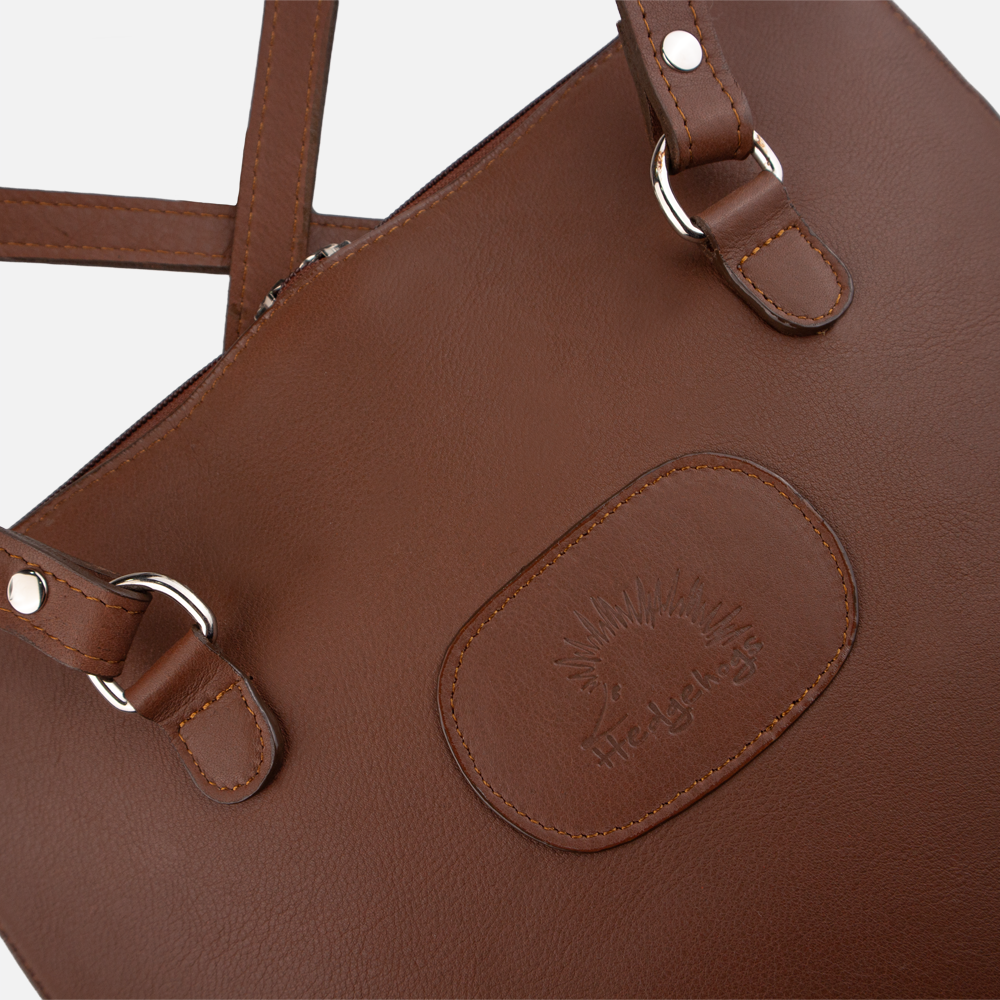Close ups view of the Hedgehogs ladies convertible backpack in chocolate leather, showing logo embossing and front strap hardware.