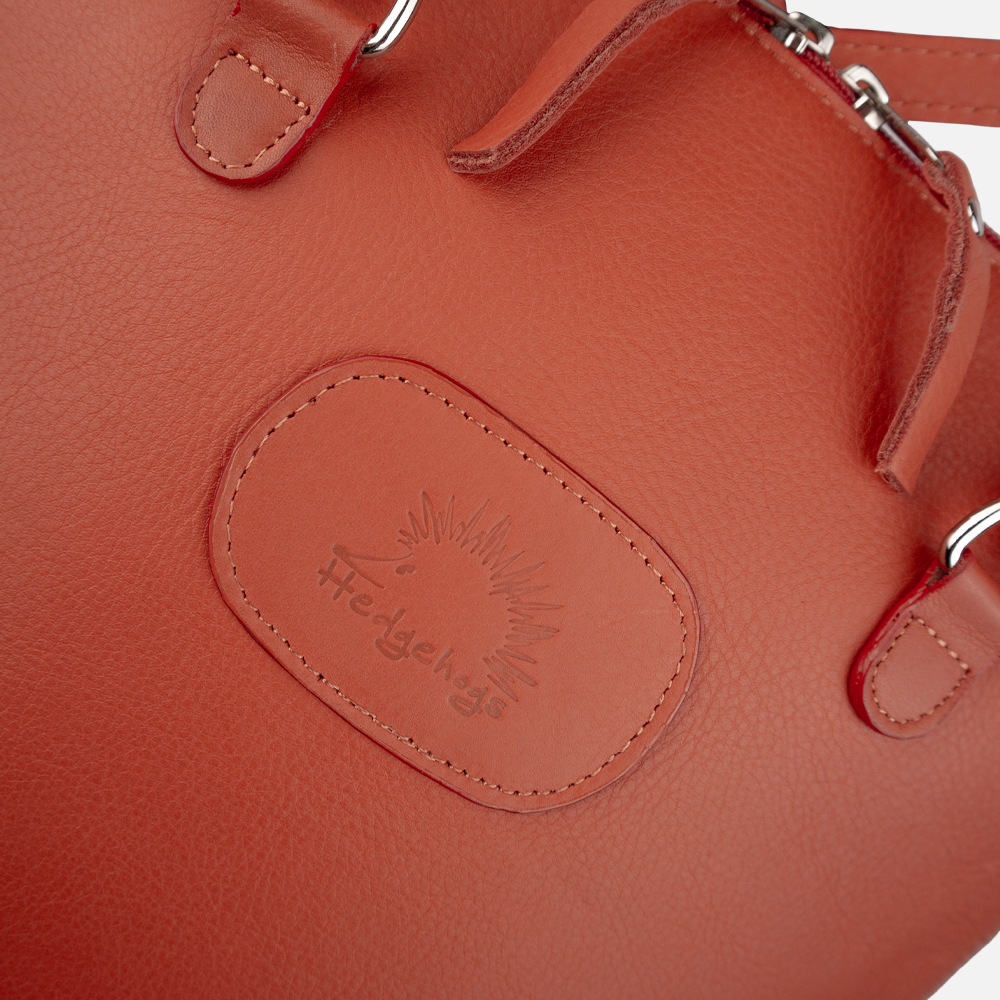 Close up view of the logo embossing on the front of the Hedgehogs ladies coral leather convertible backpack