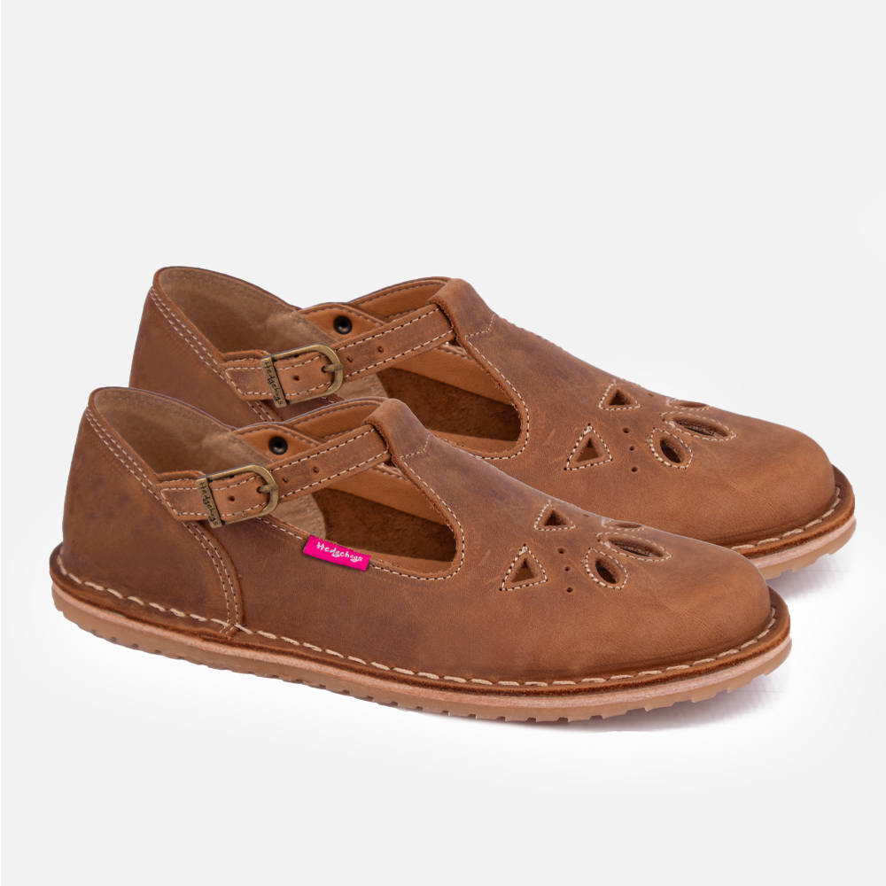 A pair of Hedgehogs Sarah shoe, a flat baby-doll style ladies leather shoe featuring feminine detailing over the toe area and t-bar and strap with a buckle closure. 